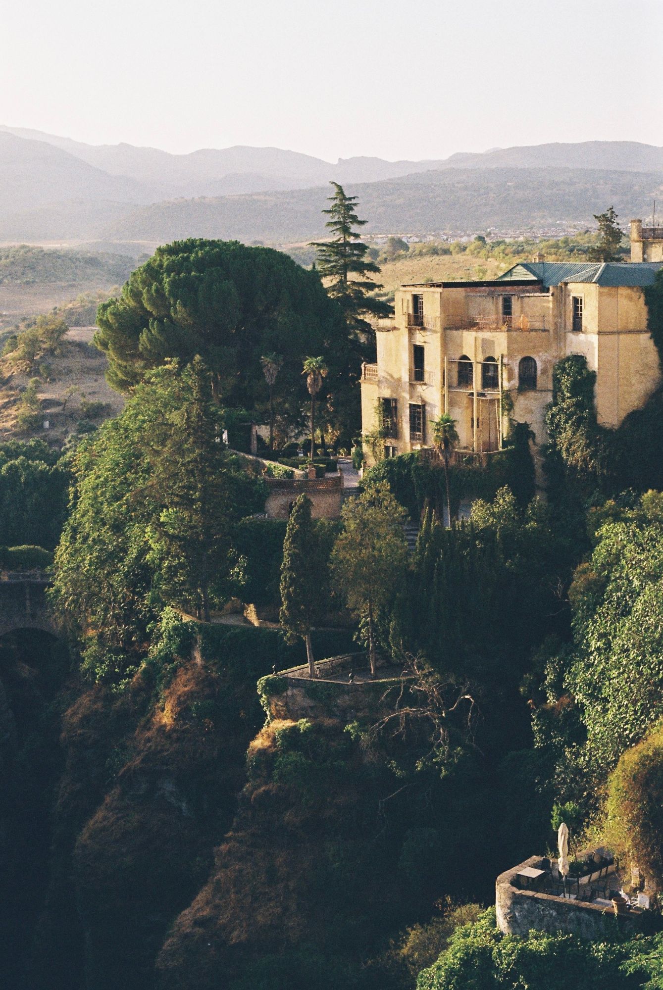 Ronda: ein ockerfarbenes Haus mit Garten am Rand einer bewaldeten Schlucht, dahinter Hügel im Abendlicht
