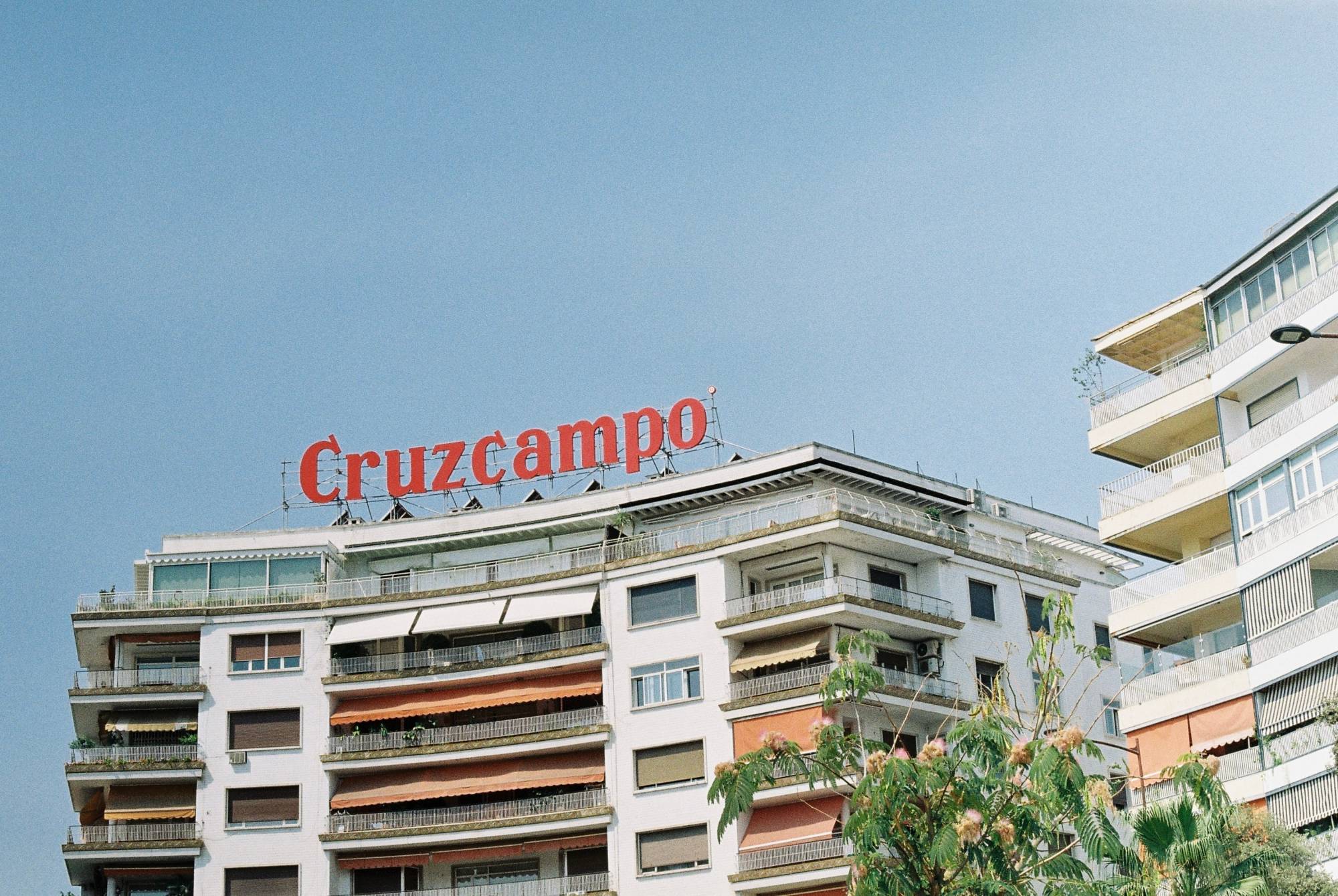 Sevilla: rote Cruzcampo-Leuchtschrift auf dem Dach eines Wohnhauses vor blauem Himmel